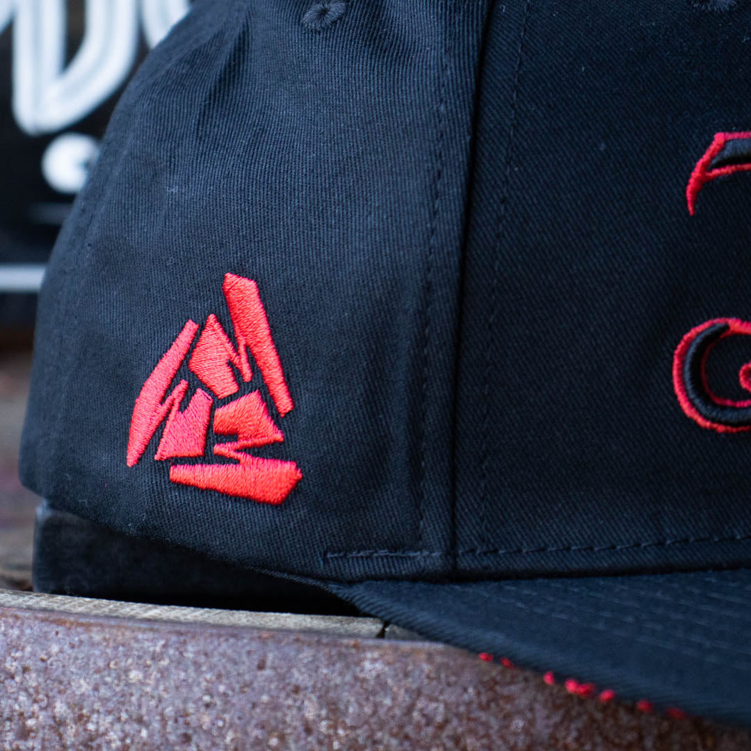 Close up of side of Menace Clothing black and red baseball hat showing red embroidered Menace Tri M logo. 