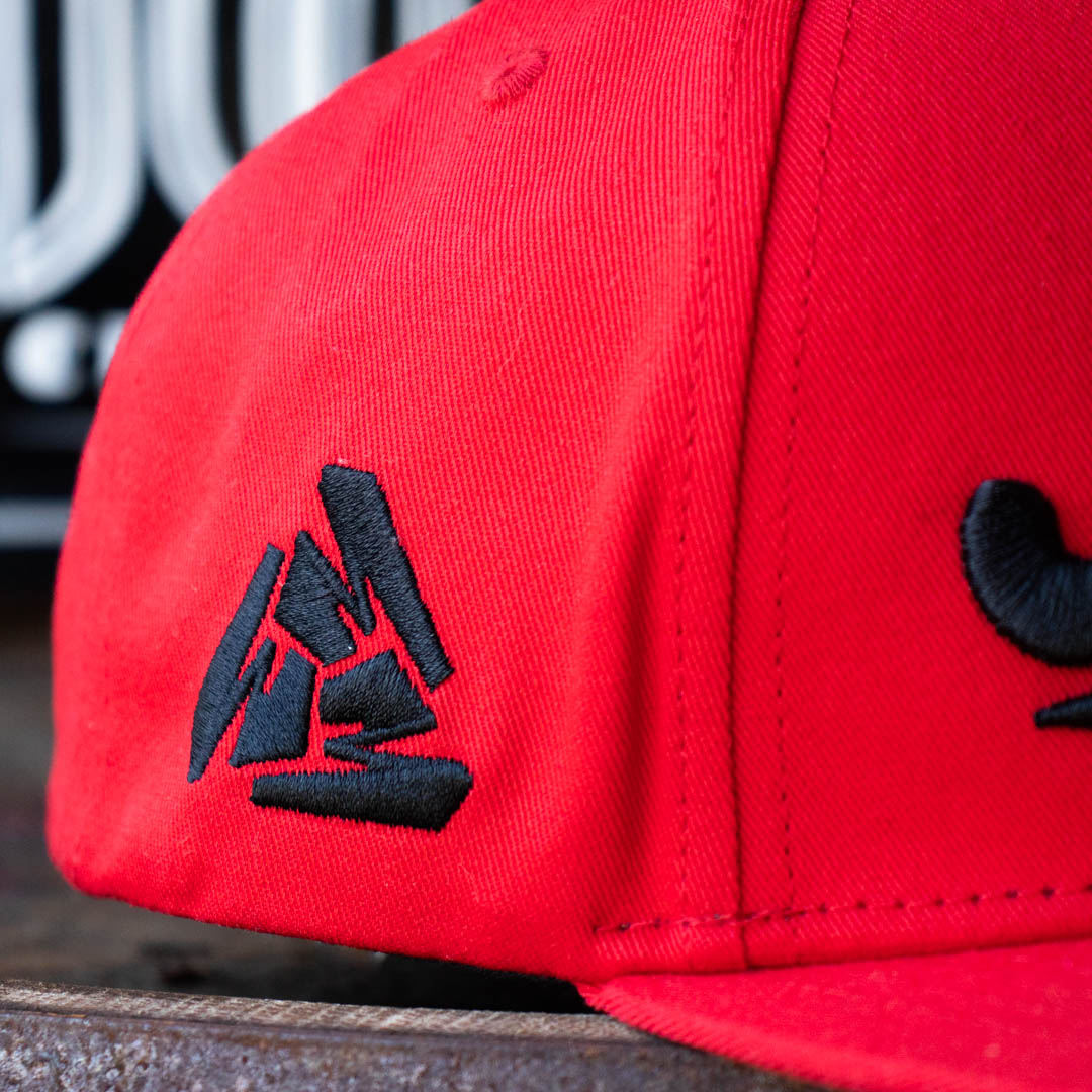 Close up of right side of Menace Clothing red baseball hat with black embroidered Menace Tri M logo.