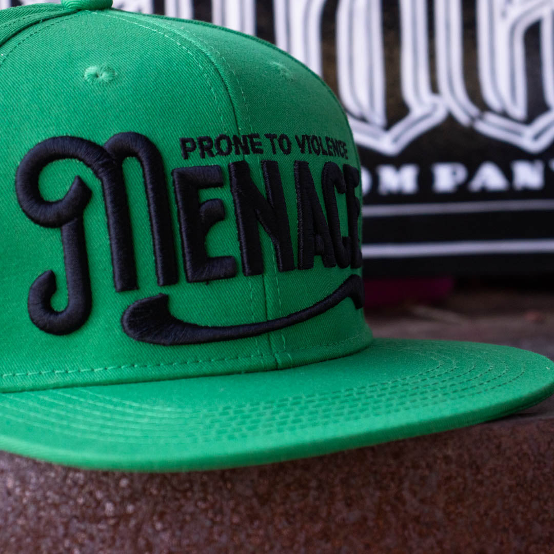 Close up of Menace Clothing green baseball hat with black puff embroidered saying Menace Prone To Violence.