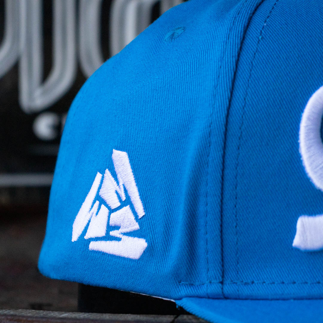 Close up of right of Menace Clothing blue baseball hat with white embroidered Menace Tri M logo.