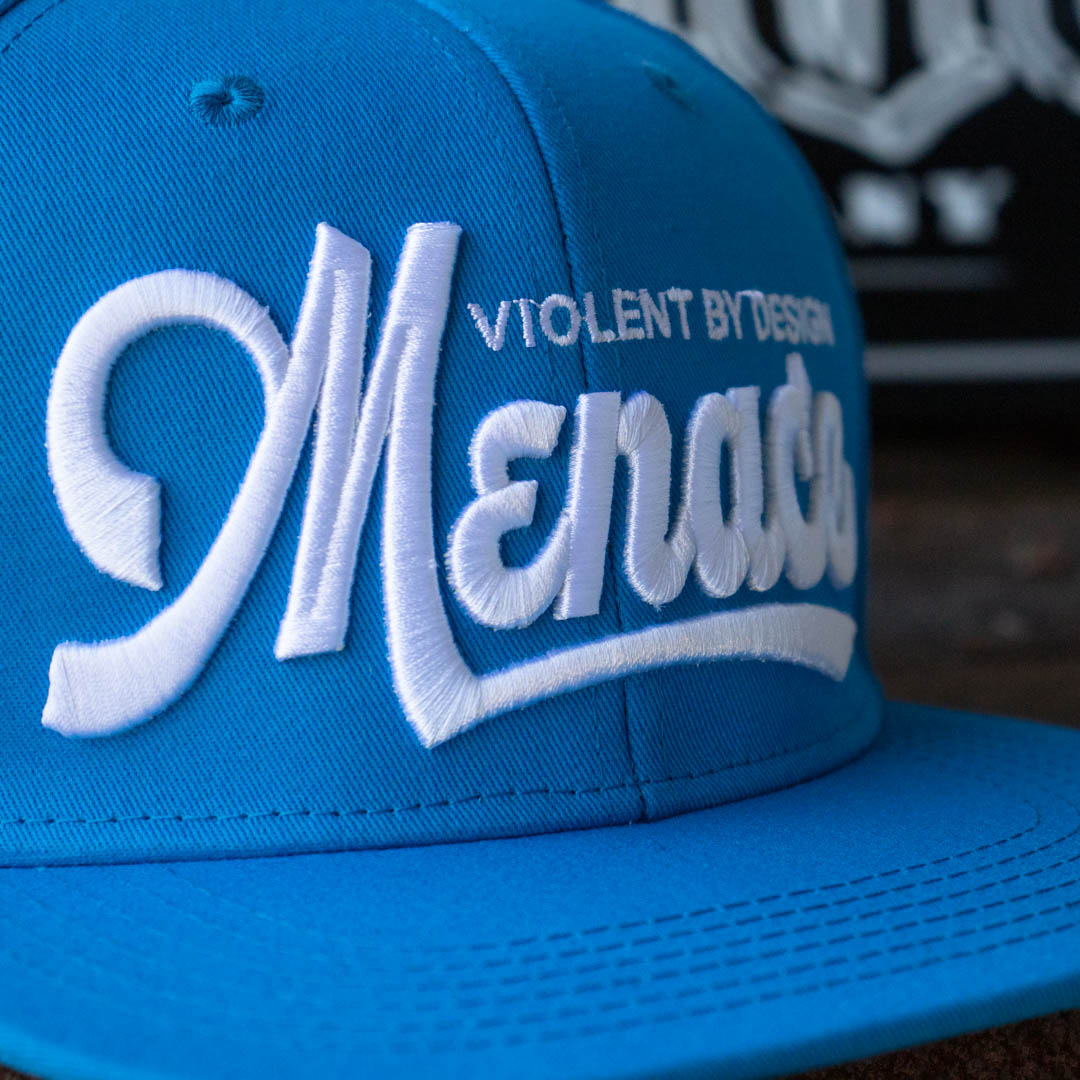 Close up of Menace Clothing blue baseball hat with white puff embroidered saying Menace Violent By Design.