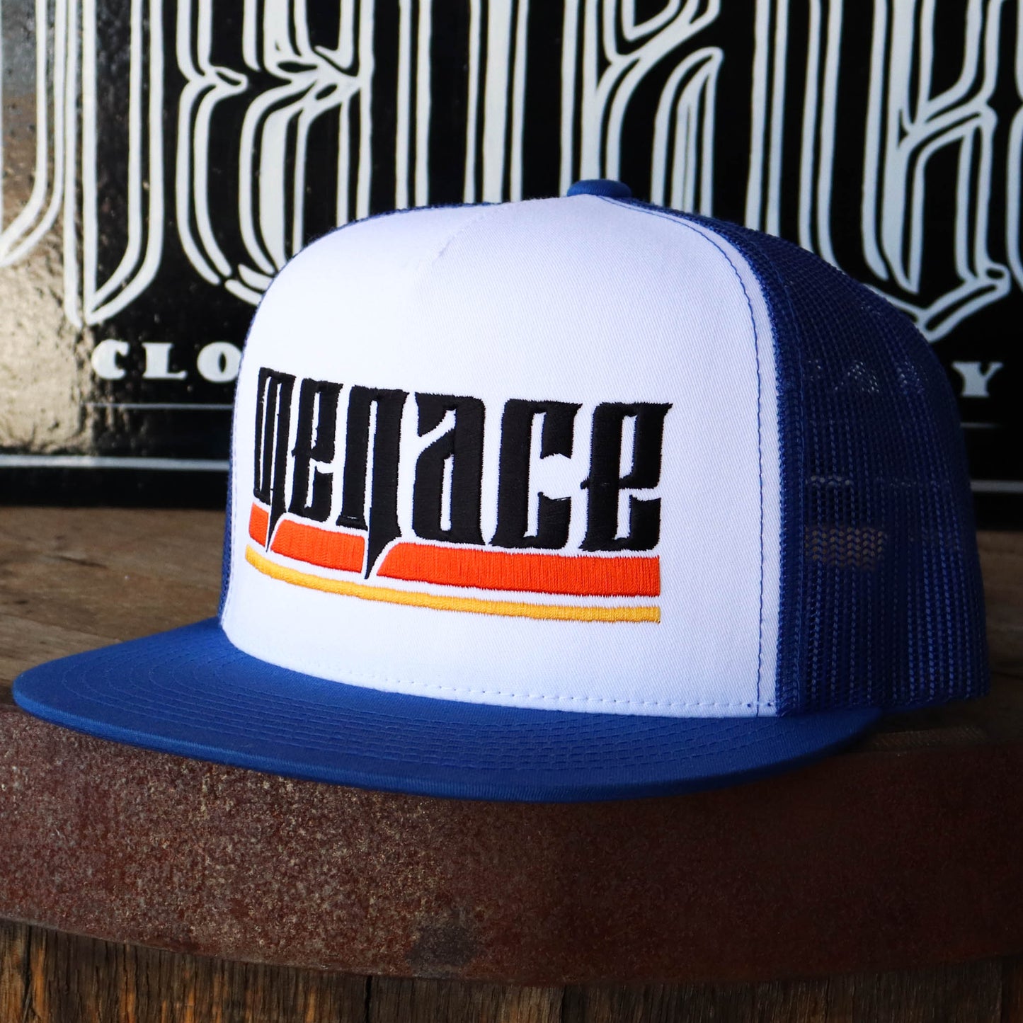 Royal blue mesh snap back hat with embroidered Menace in black, underlined by orange and yellow lines. Slightly turned to the left.