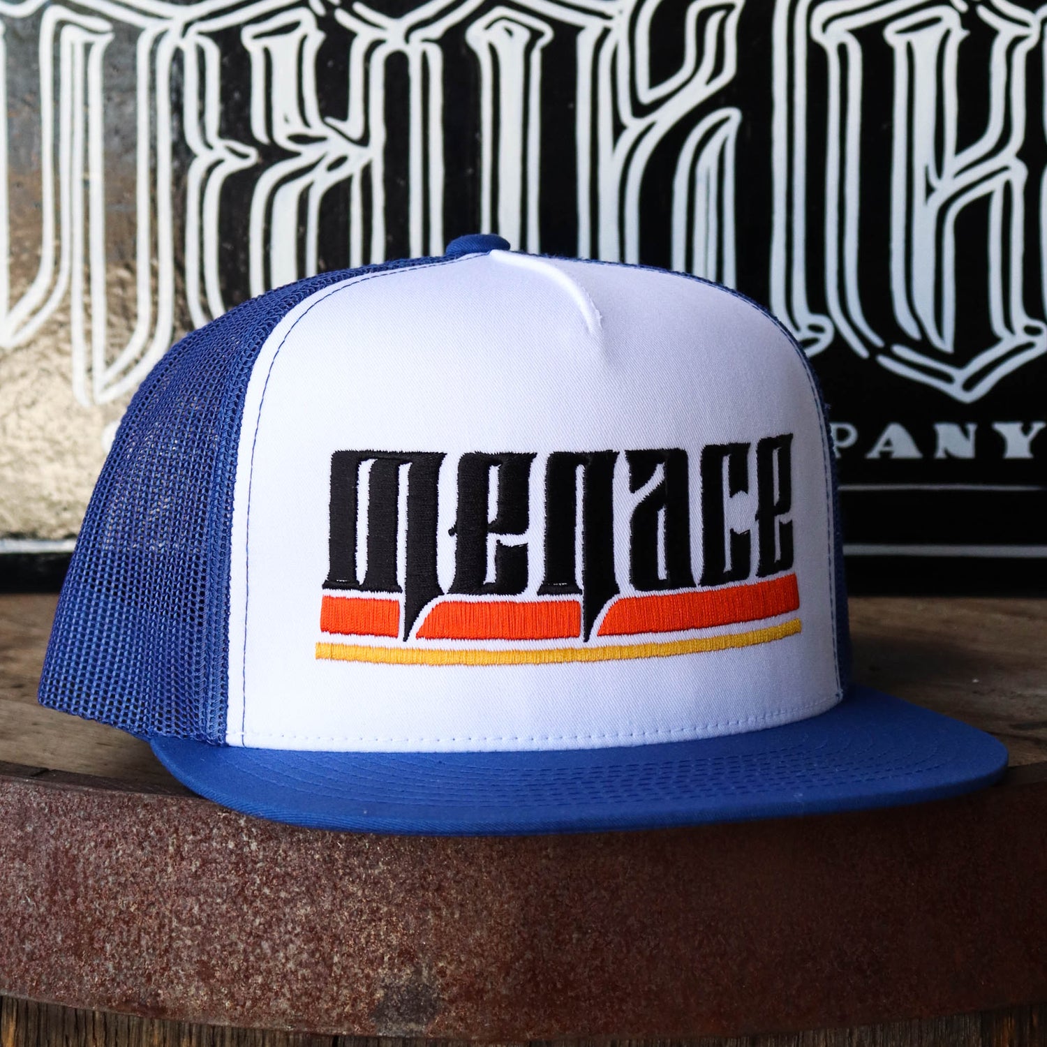 Royal blue mesh snap back hat with embroidered Menace in black, underlined by orange and yellow lines. Slightly turned to the right.